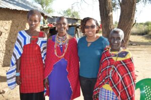4 smiling women in front of tree and Maasai Manyatta.